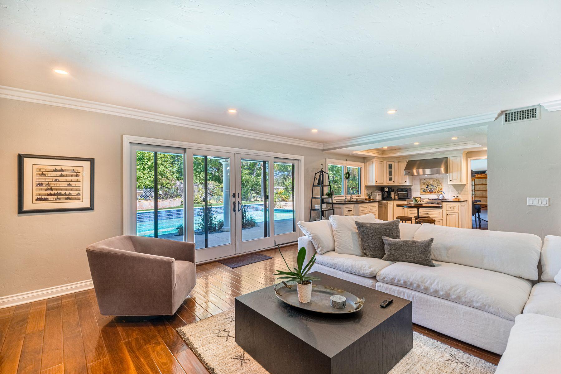 A furnished living room with pale framed glass doors overlooking a pool and garden.