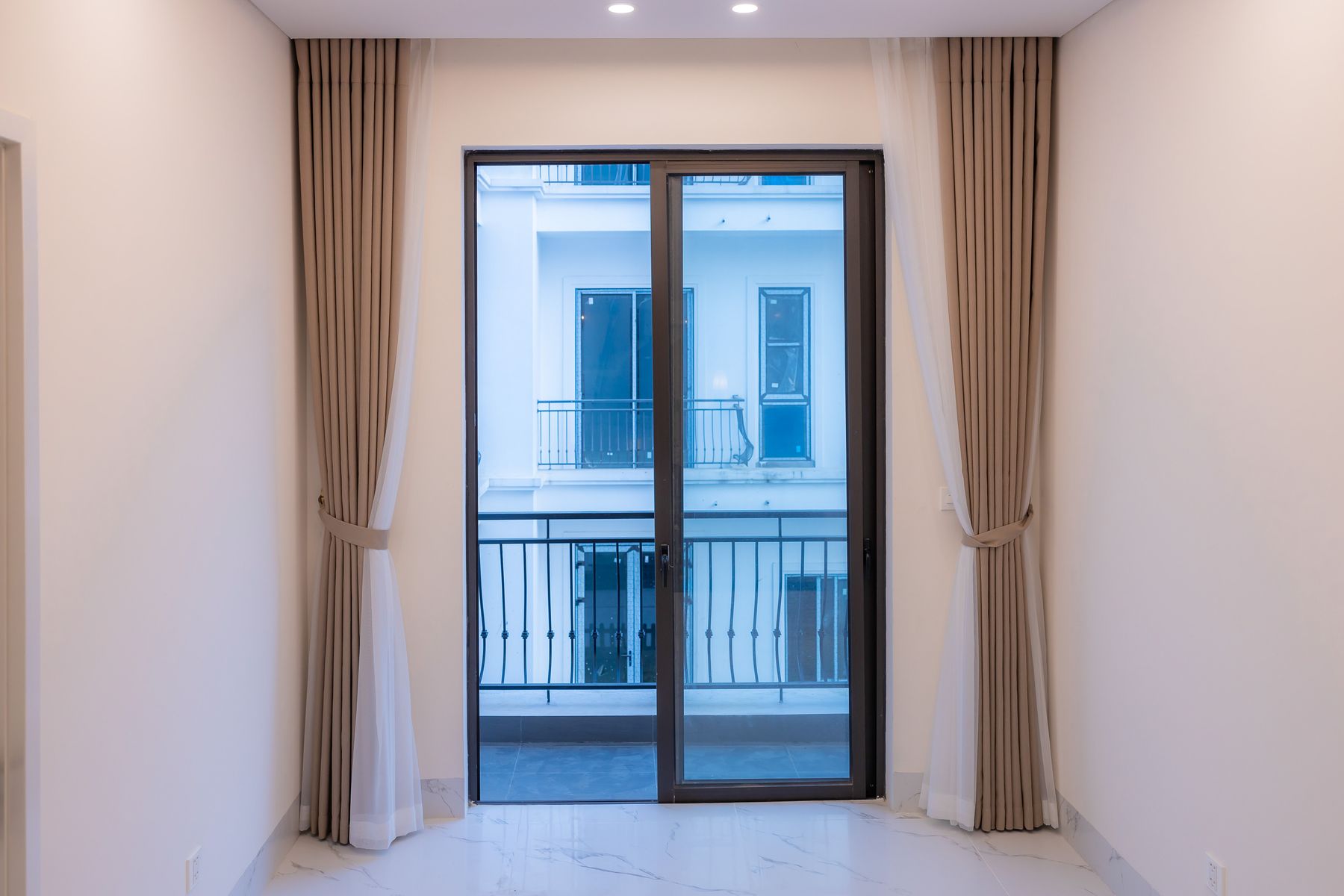 Dark framed sliding glass door opening onto a balcony, with curtains on either side.